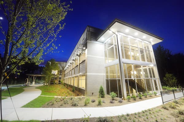 Exterior of a modern-looking building with many windows, lights, and a staircase.