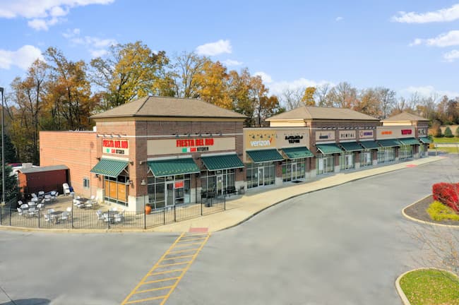 Photo of an outdoor shopping mall along a street with a restaurant and several other stores