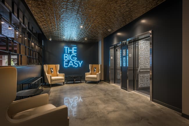 Open space with Neon sign saying The Big Easy, several tan chairs with skulls on the chair backing, and an elevator.